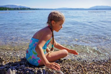 Mutlu kız eğleniyor ve taşlarla oynuyor Cenevre Gölü 'nün çakıl taşlı sahillerinde güneş ışığında mavi dağların üzerinde, çok fazla eğlence ve mutluluk, yaz tatili, seyahat ve yaz tatili, yaşam tarzı