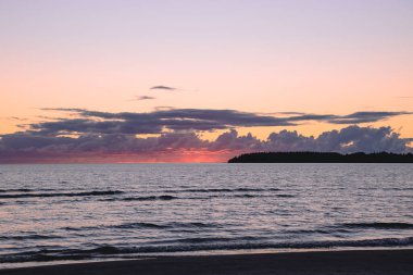 Bulutlu bir gökyüzünde denizin arka planında parlak kırmızı bir gün batımı.