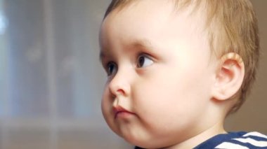 Çizgili kazaklı küçük bir çocuk odadaki bir yatağa oturur, kahverengi gözlü şirin bir bebek kameraya bakar. Yüksek kalite 4k görüntü