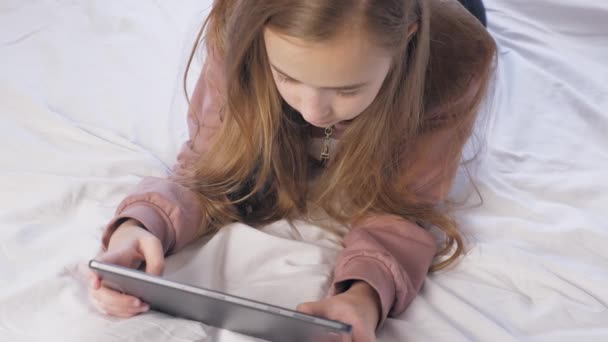 一个少女躺在一个有石碑的房间里的床上 一个玩平板电脑的女孩的全脸 从上面看高质量的4K镜头 — 图库视频影像