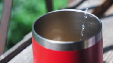 Sıcak su, ahşap pencere pervazında duran kırmızı bir termo bardağa dökülüyor. Kahve yapma süreci. Yüksek kalite 4k görüntü