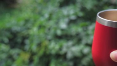 Çerçevede kırmızı kupa tutan bir kadın eli beliriyor. Arka planda yeşil bir duvar görebilirsiniz. Doğada dinlen. Yüksek kalite 4k görüntü