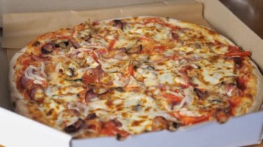 Peynirli sıcak iştah açıcı pizza, Bavyera sosisi, domates, soğan ve mantar masanın üzerindeki karton kutuda yatıyor. Yüksek kalite 4k görüntü