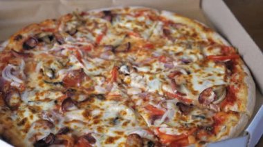 A womans hand takes a piece of hot appetizing pizza with cheese, Bavarian sausages, tomatoes, onions and mushrooms from a cardboard box. A teenage girl takes a piece of pizza. High quality 4k footage