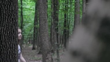 A teenage girl walks herself in the forest. A cute girl in gray jeans and a white t-shirt walks through the forest in summer. High quality 4k footage