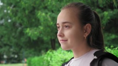 Portrait of a young beautiful girl standing in the park. A girl with her hair gathered in a ponytail enjoys the beauty of nature. High quality 4k footage