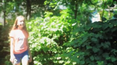 Uzun sarı saçlı genç bir kız şehrin yeşillikleri arasında yürüyor. Şortlu ve tişörtlü kız bulanıklaşıyor. Yüksek kalite 4k görüntü