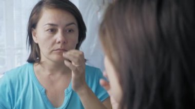 Caucasian woman stands in front of a mirror and runs her hand over her face. An adult girl looks at herself in the mirror in the morning. High quality 4k footage