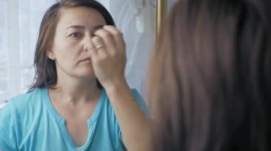 A Caucasian woman stands in front of a mirror and runs her hand through her hair and examines herself. An adult girl looks at herself in the mirror in the morning. High quality 4k footage