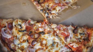 Hot appetizing pizza with cheese, Bavarian sausages, tomatoes, onions and mushrooms lies in a cardboard box on the table. Appetizing pizza lies in a box, a few pieces of pizza are missing. The opened
