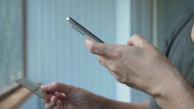 Bir kadın tarar, telefon kullanarak kart numarasını okur. Kız telefonu kullanarak alışveriş yapıyor. İnternetten satın almak. Kadınların elleri kapalı olsun. Yüksek kalite 4k görüntü