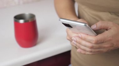The girl stands in the kitchen and holds a phone in her hands. A woman makes purchases on the Internet using her phone. High quality 4k footage