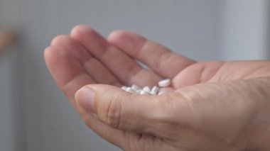 A handful of heart-shaped pills lie in a womans palm. The girl examines the mountain of pills that she has in her hand. A woman is standing in her house, apartment with medicine in her hand. High