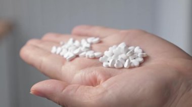 A handful of heart-shaped pills lie in a womans palm. The girl examines the mountain of pills that she has in her hand. A woman is standing in her house, apartment with medicine in her hand. High