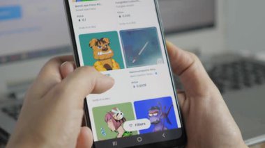 The girl looks through the nft auction in the browser on the smartphone. A woman makes a purchase of nft pictures. Online NFT marketplace selling Non-fungible token on a smartphone. Artistic NFT Non