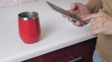 The girl stands in the kitchen and holds a phone in her hands. A woman makes purchases on the Internet using her phone. High quality 4k footage
