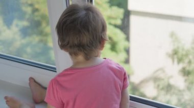 Küçük bir çocuk pencere pervazında oturur ve pencereden şehre bakar. İhmalkârlık ve sorumsuzluk kavramı. Bebek yüksek katlı bir binanın penceresinden dışarı bakıyor. Yüksek kalite 4k