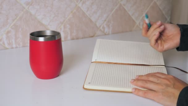 这个女孩坐在厨房桌子边喝热咖啡时 在笔记本上写了个字条 女人的手紧握着 一个女人喝了一杯热饮 然后在日记中写下了她的想法 高质量4K — 图库视频影像