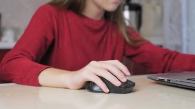 Kırmızı kazaklı genç bir kız mutfaktaki sandalyede otururken dizüstü bilgisayarda oyun oynuyor. Çocuk ev ödevi yapmak yerine dizüstü bilgisayarda oynuyor. Yüksek kalite 4k görüntü