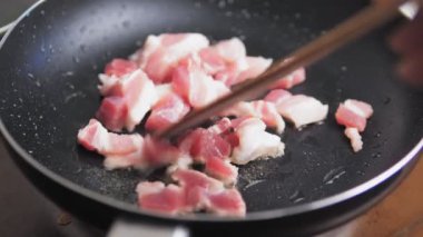 Kişi çiğ domuz pastırmasını ahşap bir spatulayla karıştırıyor. Tavada yemek pişirmek. Domuz eti sıcak tavada kızartılır. Yüksek kalite 4k görüntü