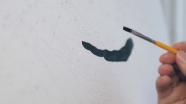 Bir kadın bir resmi numaralarla boyar. Kız çizim için bir fırça tutuyor ve siyah akrilik boyalarla bir resim çiziyor. Yüksek kalite 4k görüntü