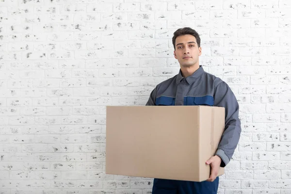 Confident male from moving service holding box beside white brick wall background