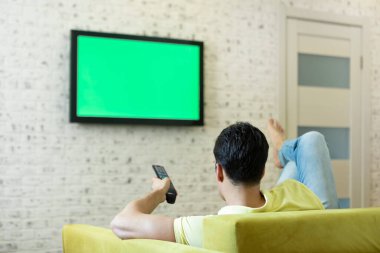 Kanepede oturan ve televizyon izleyen bir adam. Yeşil ekran konsepti