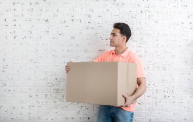 Beyaz tuğla duvarın önünde ağır kutu taşıyan yakışıklı bir adam.