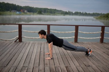 Genç sporcu adam doğa eğitimi alıyor. Ikın ve sisli göle yakın tahtaya çık.