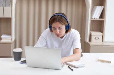 Kulaklıklı genç ve çekici bir kadın evde internetten ders çalışıyor. Uzaklık eğitimi kavramı