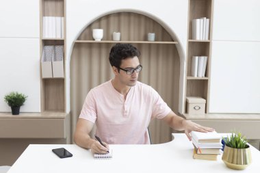 Masada bir yığın kitapla oturan genç yakışıklı öğrencinin portresi. Sınav konsepti için eğitim ve hazırlık