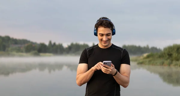 Handsome sporty man wearing headphones and listening to music after jogging on the nature. Relaxation and resting concept