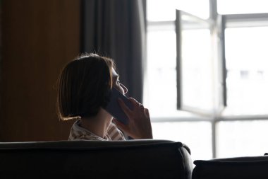 Kanepede oturan ve evdeki cep telefonuyla konuşan kadın siluetinin arkası.