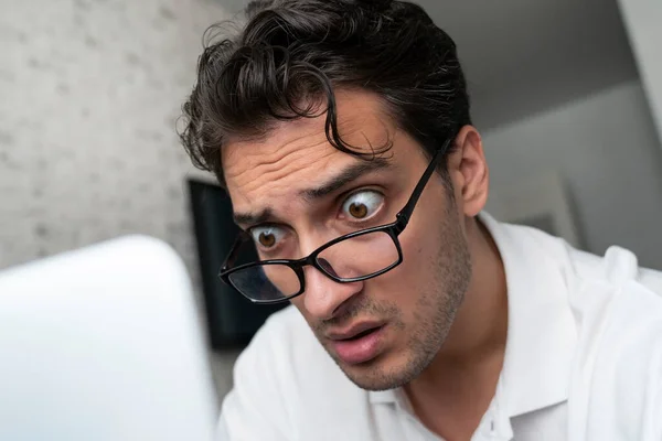 Close up portrait of shocked man with bugged eyes looking at laptop