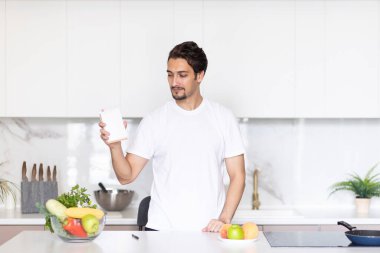 Genç, yakışıklı ve zinde bir adam mutfakta masada oturuyor ve diyet planını deftere yazıyor. Masanın üzerindeki meyve ve sebzeler de onun istihkakına dahil.