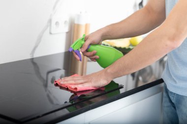 Erkek ellerinin şişe spreyi tutarken ve sobayı temizlerken yakın çekim.