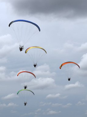 A group of colorful powered paragliders flying in the blue sky with clouds in the background clipart