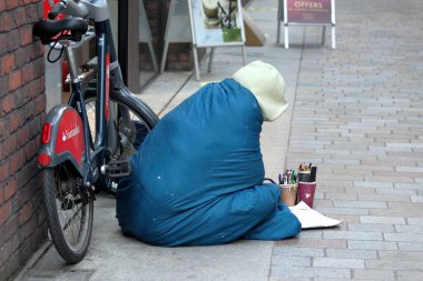 London, UK - Nov 21, 2021: homeless poor man painting while sitting on a pavement.