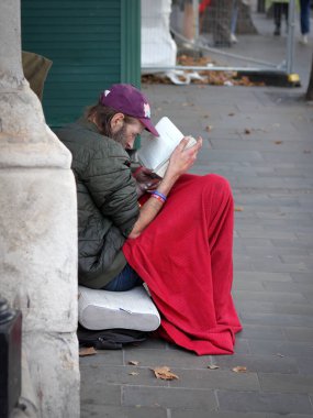 London, UK - Sep 11, 2021: Homeless man reading a book, sitting on a pavement