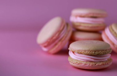 Mor bir zemin üzerinde pembe tereyağı kremalı kurabiyeler ve kopyalama alanı