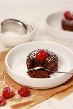 Ahududu ve beyaz mermer kaplı beyaz bir tabakta çikolatalı lave keki.