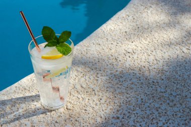 a glass of water with lemon, summer hat and sunglasses at the pool