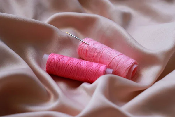 close up of a silk with pink sewing coil thread and needle