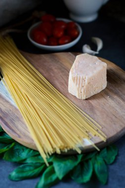 close up of spagetti and parmesan cheese on wooden board, blurred background with tomatoes and garlic 