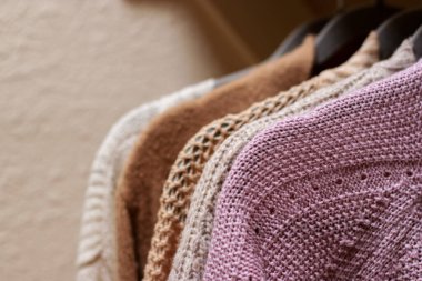 close up of pastel warm knitted cardigan sweater hanging in the closet. Cozy fall and winter wardrobe.
