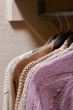close up of pastel warm knitted cardigan sweater hanging in the closet. Cozy fall and winter wardrobe.