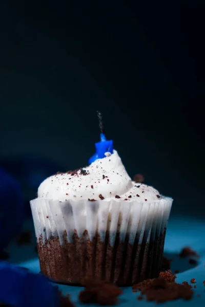 chochocolate cupcake with white buttercream and blue candle, dark background and blue ribboncolate cupcake with white buttercream and blue candle, dark background and blue ribbon. High quality photo