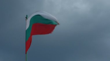 Kara bulutlara karşı rüzgarla oynayan Bulgaristan bayrağı
