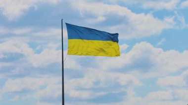 The flag of Ukraine flutters beautifully in the wind against a blue sky with clouds. Large flag on a flagpole in the Kharkiv city