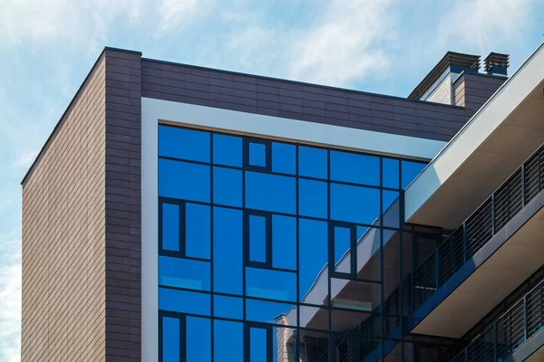 The top of the new building against the backdrop of the blue sky. Residential or office building with a facade of mirror windows. Brick wall and balconies with railing